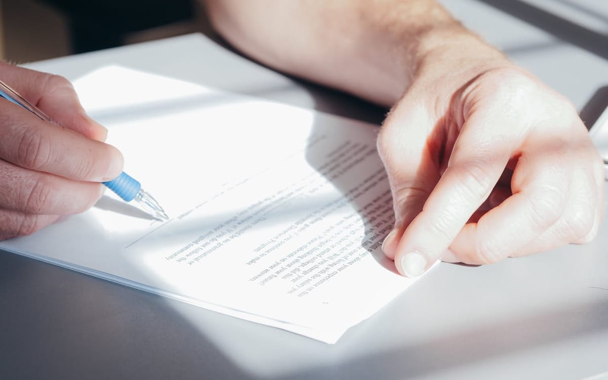 Hands signing an employment document with a pen on a sunlit desk — the contract and statutory paperwork behind a first hire in Hong Kong