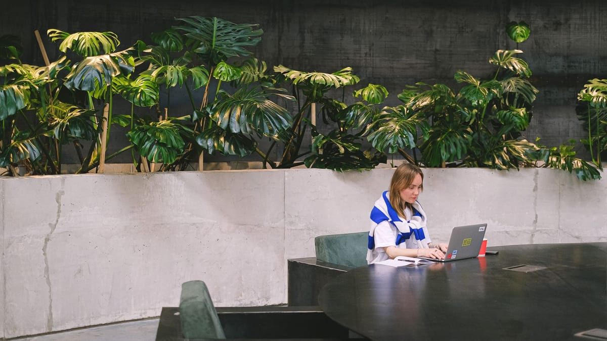 Un professionnel indépendant de sa localisation travaillant sur un ordinateur portable dans un espace lumineux et végétalisé — le « travail depuis n'importe où » d'un freelance qui facture des clients du monde entier