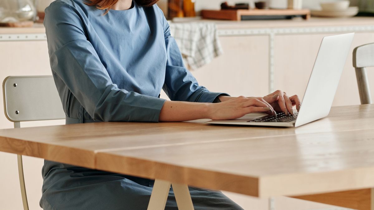 Une fondatrice tapant sur un ordinateur portable à un bureau en bois épuré — pilotant une activité tournée vers l'international depuis un espace de travail à domicile