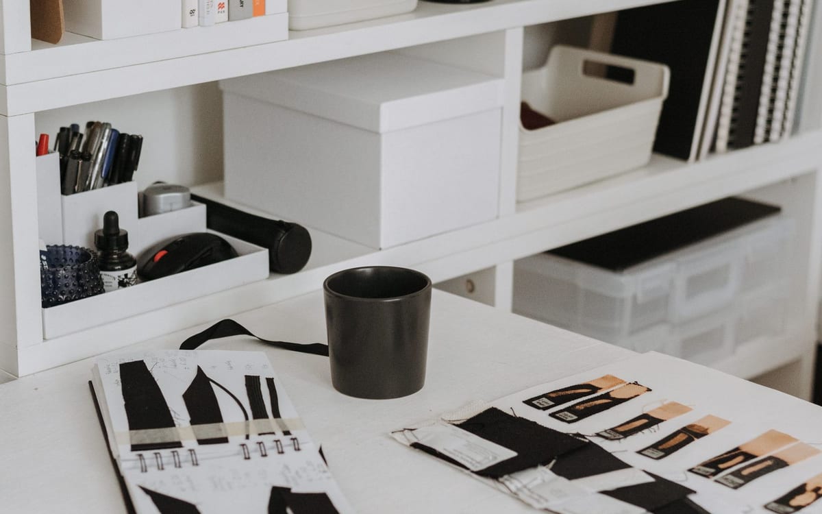 A bright design studio worktable with fashion sketches, fabric swatches, brushes and pens on open shelving — the kind of creative work and brand assets a Hong Kong company can hold in one place