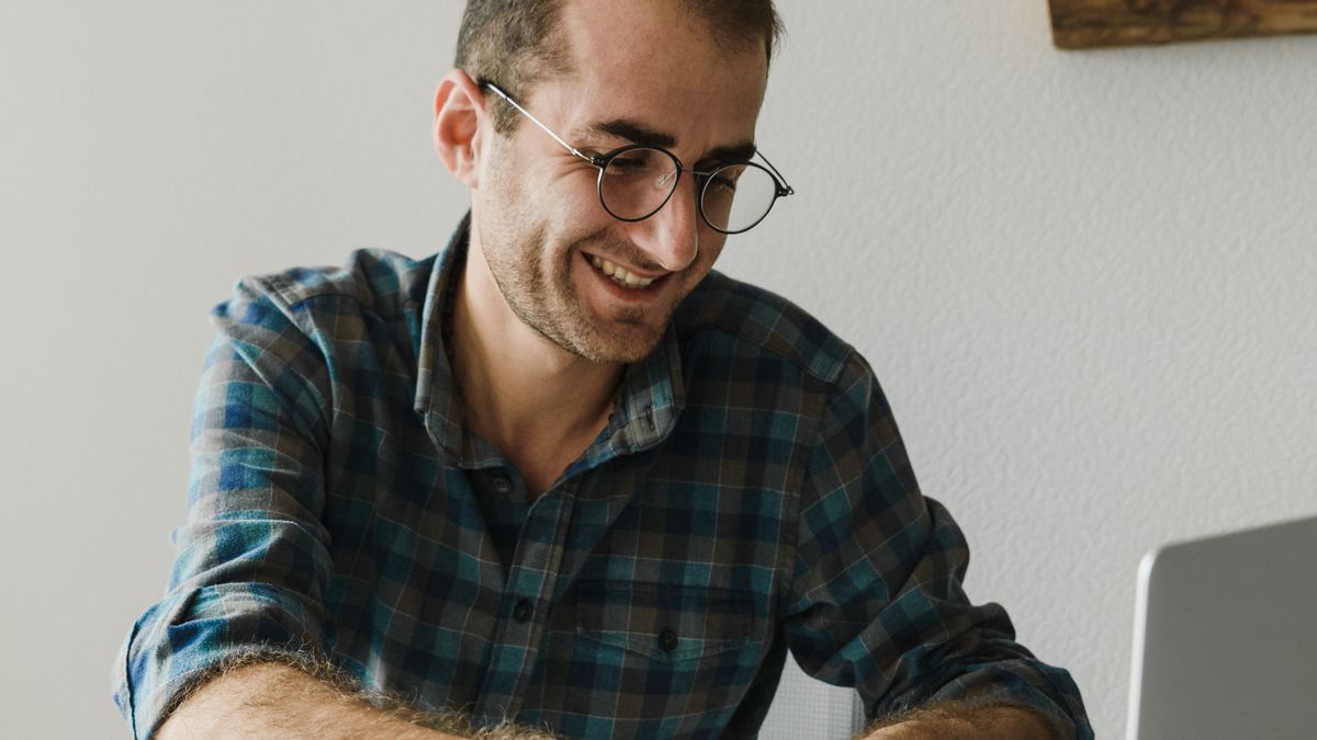 A founder smiling while working on a laptop at a home-office desk — building an internationally-facing business base