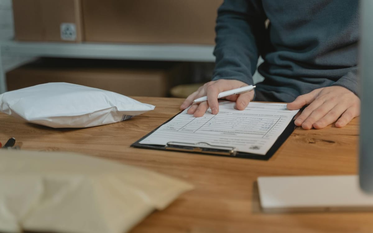 Hands completing a shipping document with a pen at a desk beside a packed parcel — the documentary paperwork a Letter of Credit is paid against