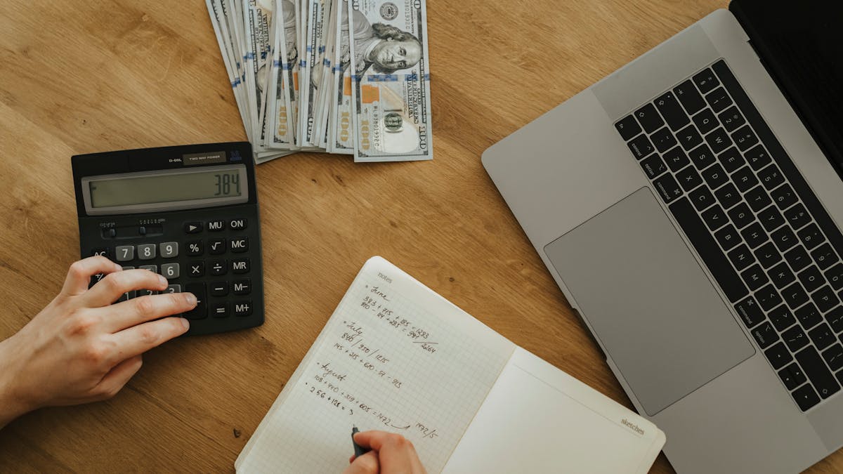 Vue de dessus des mains d'un fondateur sur une calculatrice, avec un cahier de chiffres mensuels, des billets et un ordinateur portable sur un bureau en bois — la revue trimestrielle de conversion en pratique