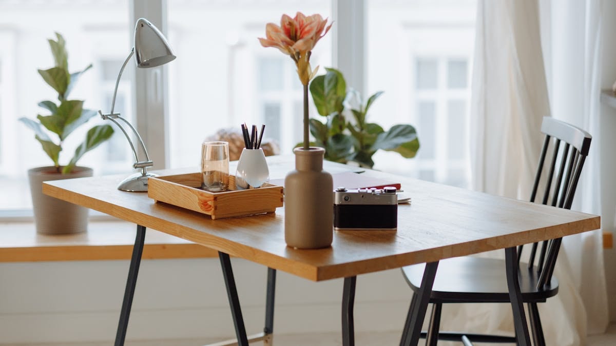 A tidy home-office desk by bright windows with a lamp, plants and a notebook tray — the kind of remote setup a non-resident founder runs a Hong Kong company from