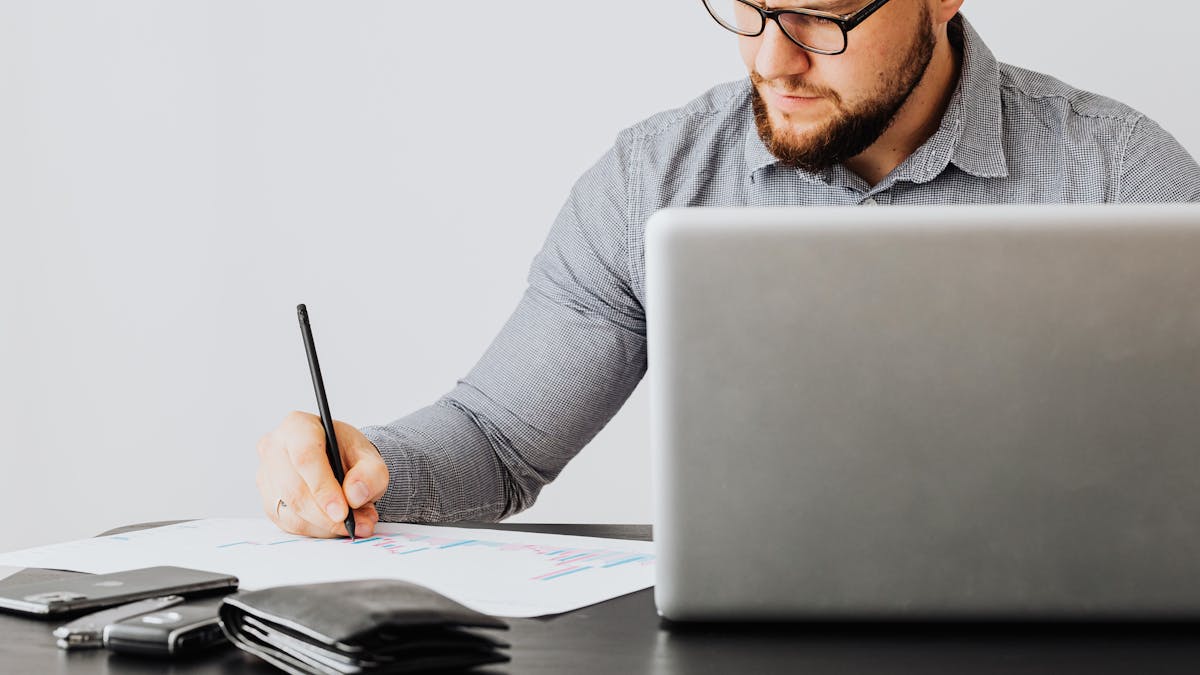 Un fondateur à lunettes annotant un graphique de performance à côté d'un ordinateur portable — analysant les coûts et compromis de deux options de constitution