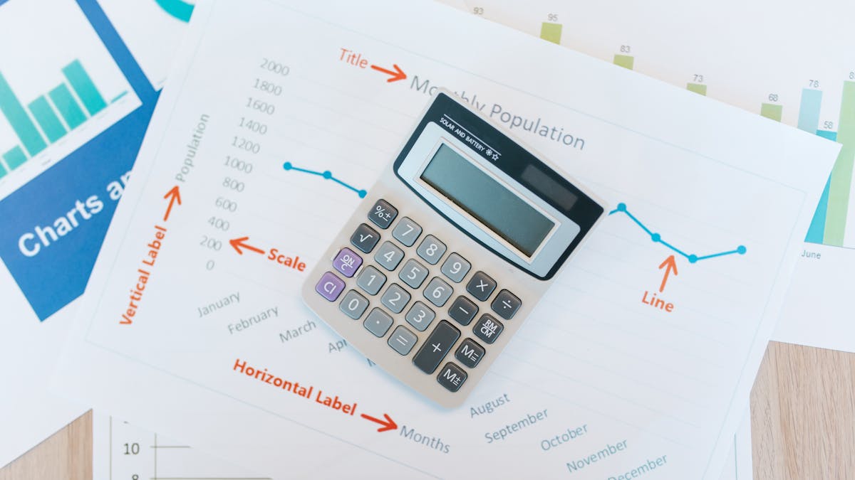 Une calculatrice posée sur des graphiques financiers imprimés — faisant les comptes du coût d'une société américaine par rapport à une société à Hong Kong